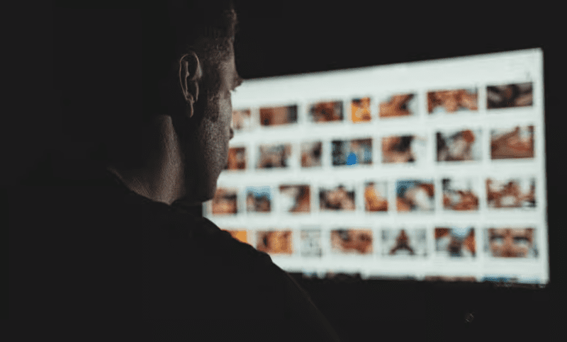 cybersexe - homme regardant un écran avec des vignettes de vidéos pornos.